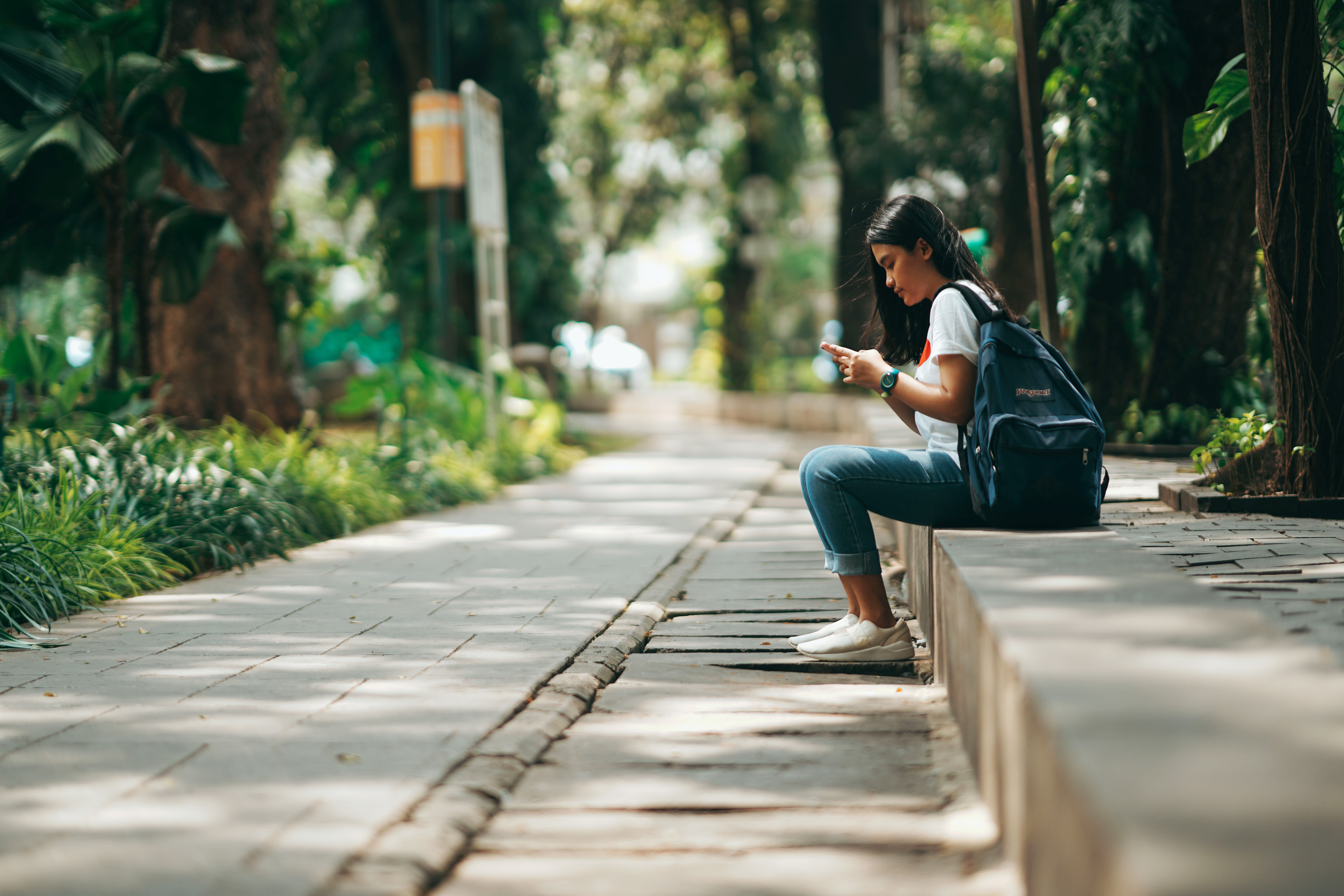 A woman sits on a concrete bench and looks at her phone.